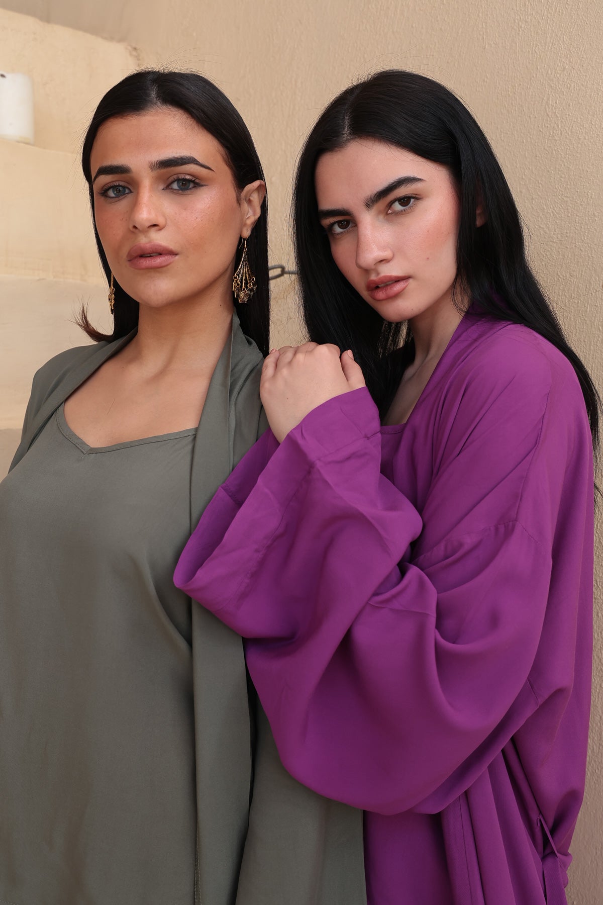 Image of Two women standing side by side, one in a gray outfit and the other in a purple outfit, against a neutral background.