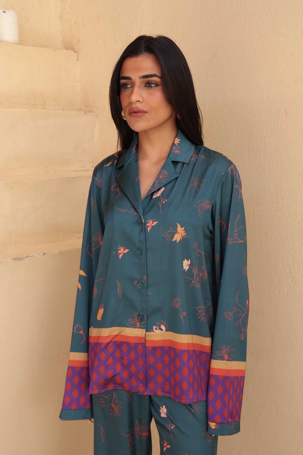 Image of Woman wearing a teal patterned outfit against a beige wall