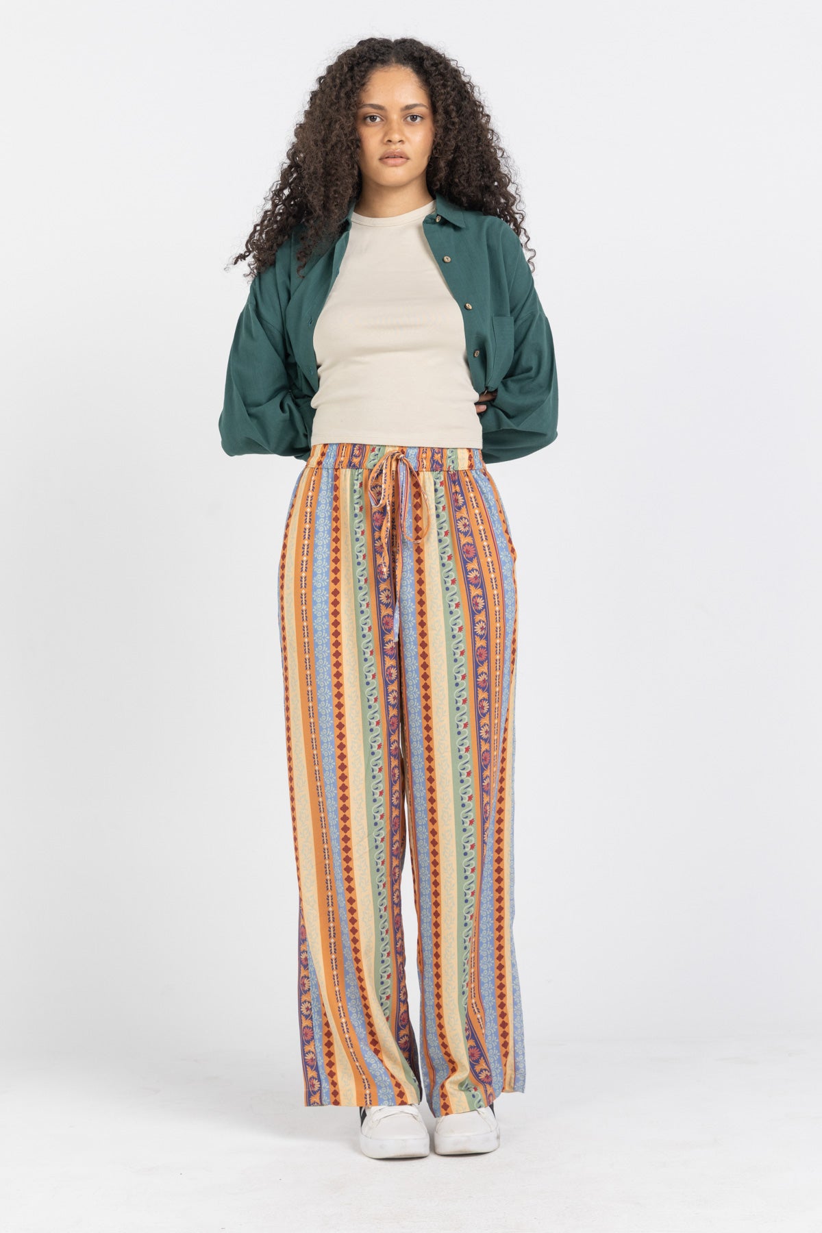 Woman wearing a green jacket, beige shirt, and colorful striped pants on a white background